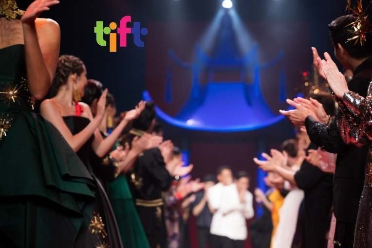 Picture from a Fashion week event where models gather around a designer and applaud the work.